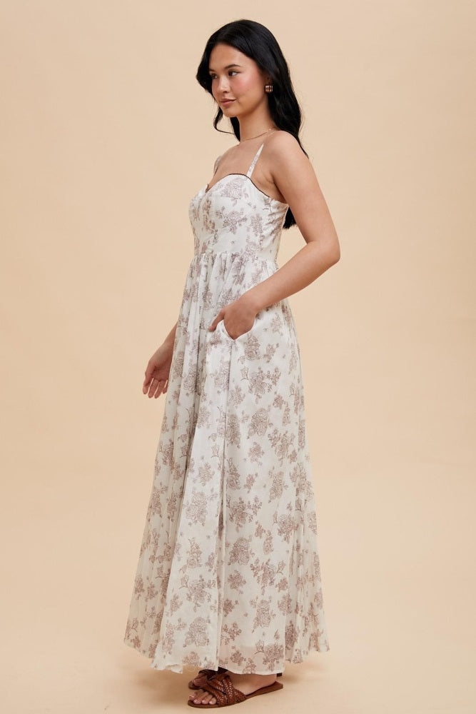 woman wearing a floral print maxi dress with a fitted bodice and side pockets, styled with brown sandals