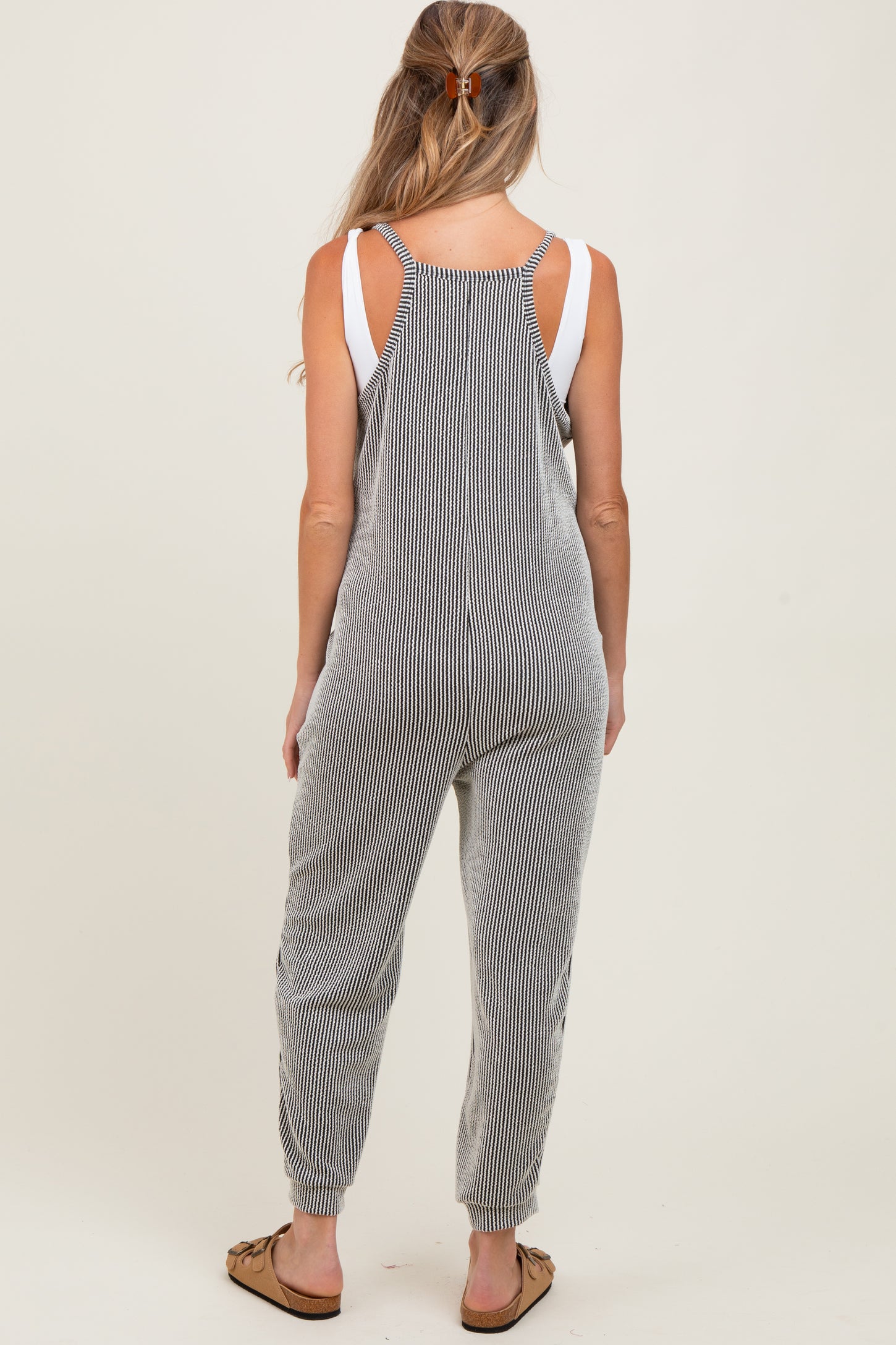 woman wearing a striped maternity jumpsuit with adjustable shoulder straps, showing a relaxed fit and tapered legs