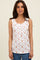 woman wearing a white sleeveless top with a floral print and button details, styled with blue jeans