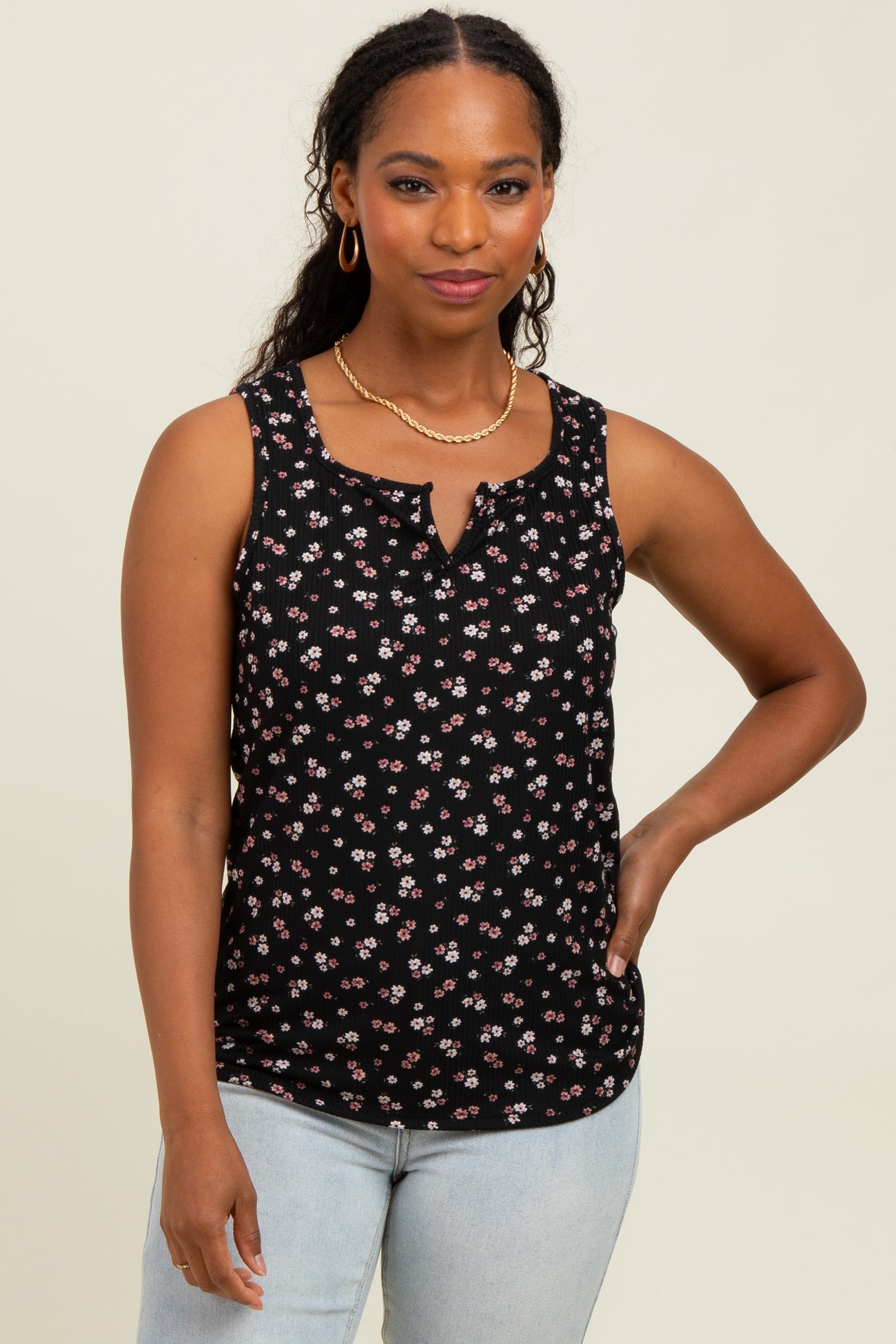woman wearing a black sleeveless top with a floral print and a button detail, paired with light blue jeans