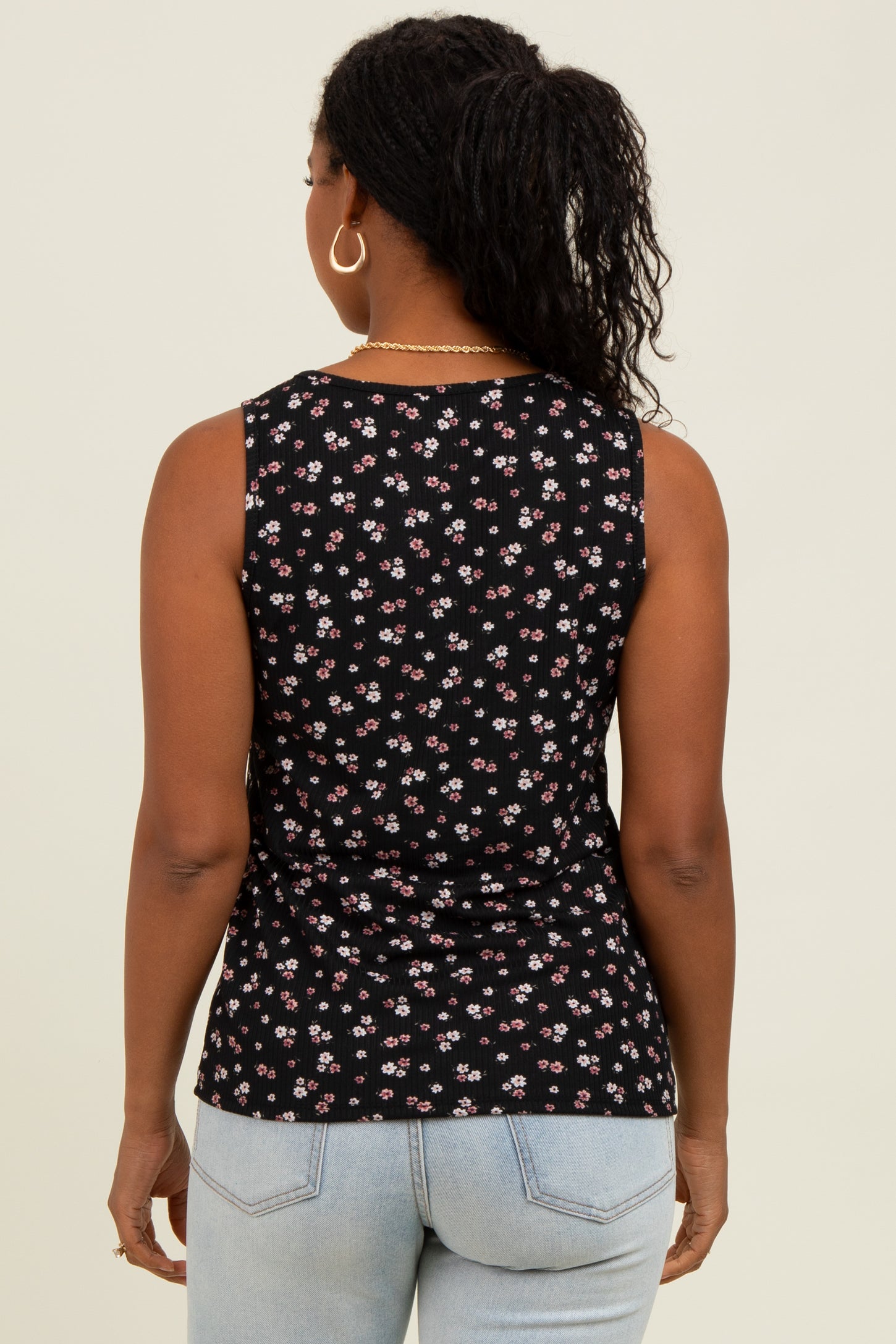 woman wearing a black sleeveless top with a floral print, viewed from the back, paired with light blue jeans