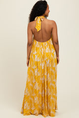 woman wearing a yellow halter neck maxi dress with a backless design and white tropical leaf print