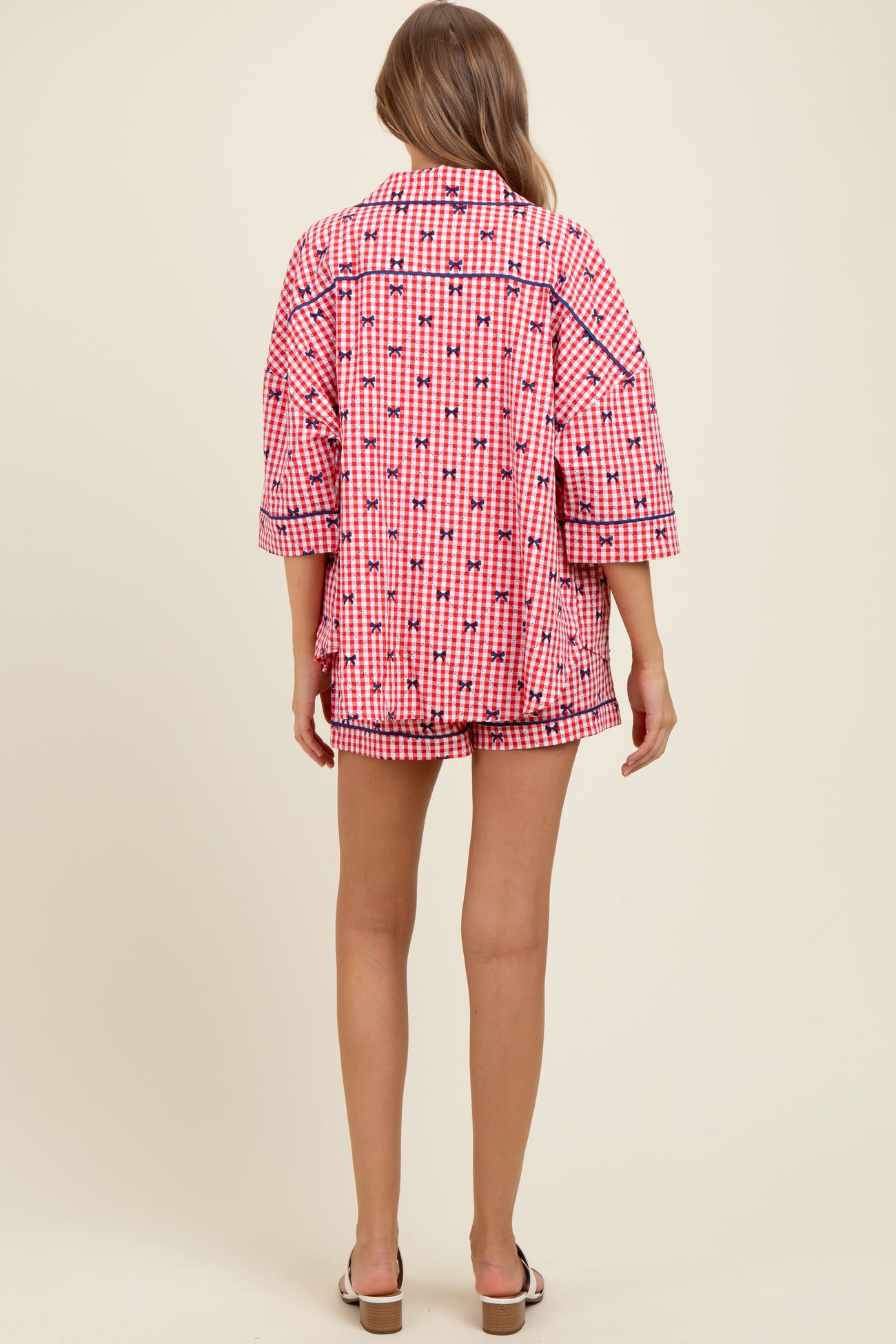 woman wearing a pink and white checkered maternity pajama set with oversized top and shorts, showing a baby bump from the back