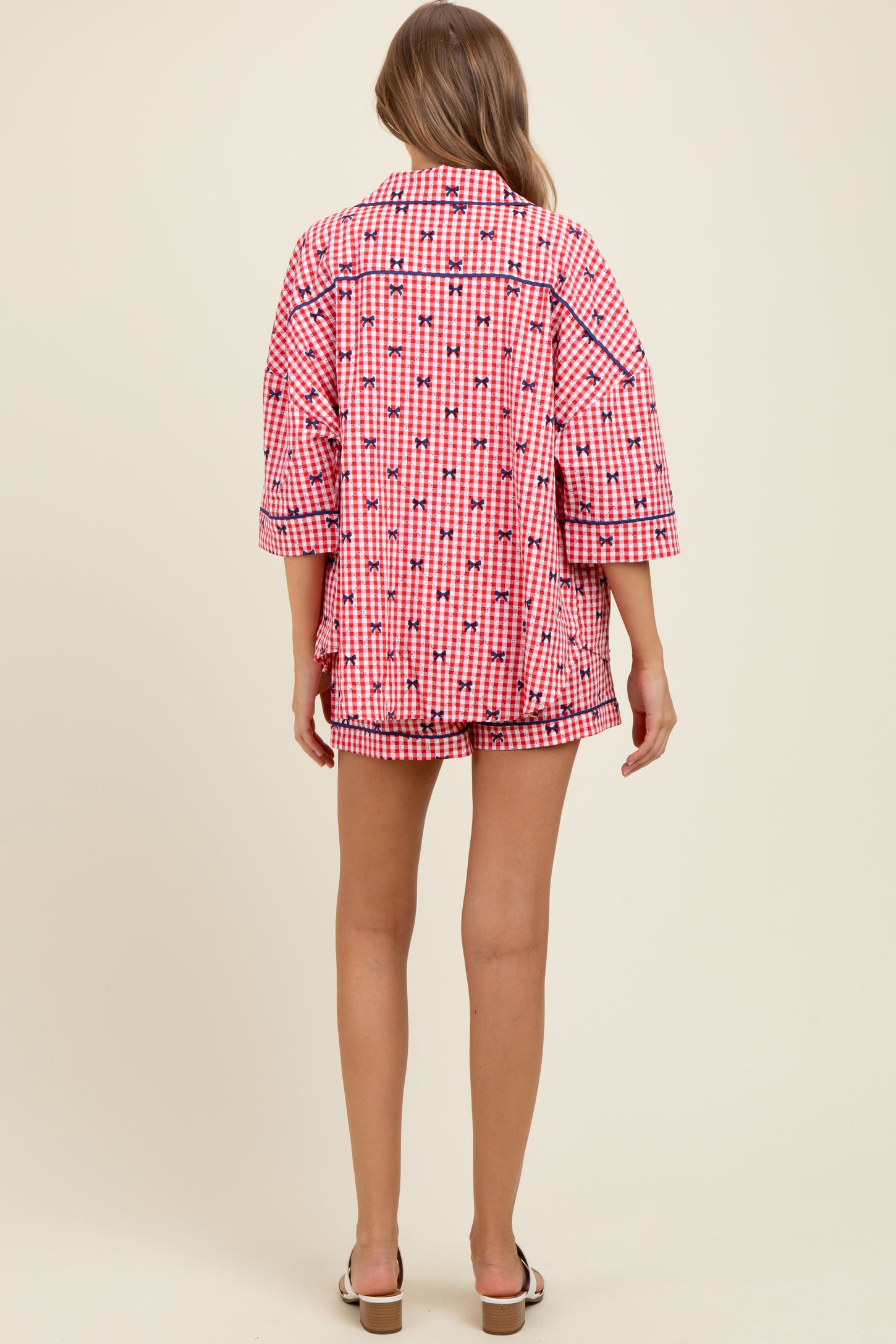 woman wearing a pink and white checkered maternity pajama set with oversized top and shorts, showing a baby bump from the back