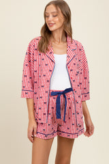 woman wearing a red and white gingham printed maternity pajama set with shorts and a button-up shirt