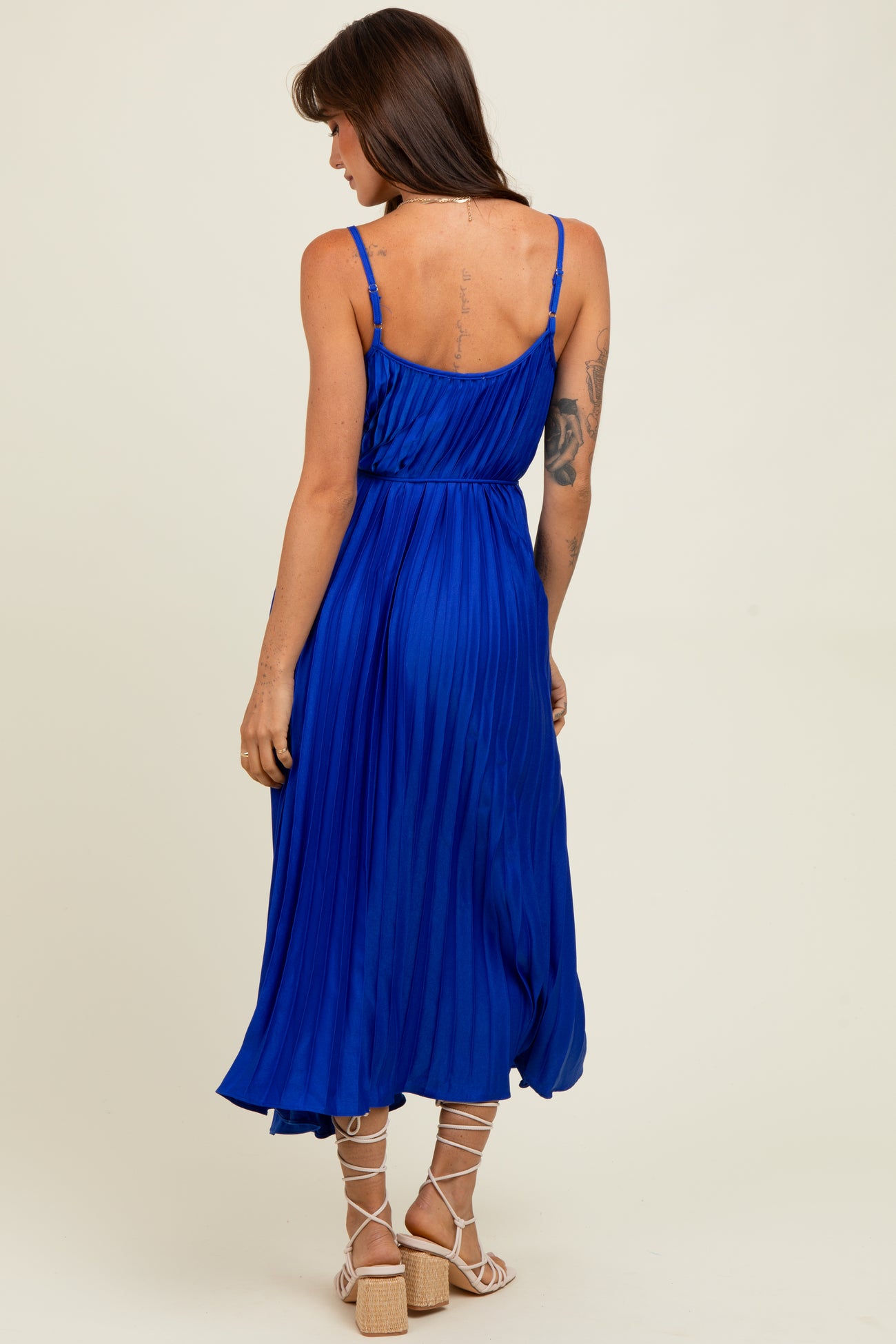 woman wearing a pleated royal blue midi dress with thin straps and a cinched waist, seen from the back