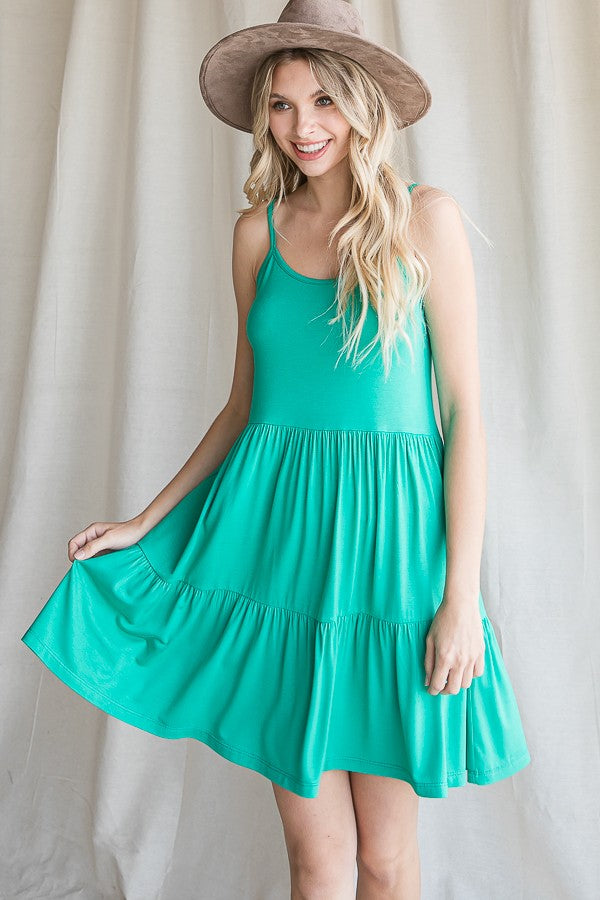 woman wearing a sleeveless green tiered sundress and a wide-brimmed hat, smiling while posing