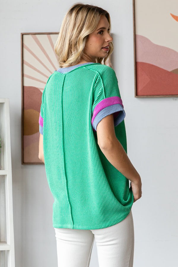 woman wearing a green ribbed oversized top with purple and pink striped sleeves, viewed from the back
