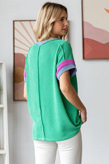 woman wearing a green ribbed oversized top with purple and pink striped sleeves, viewed from the back