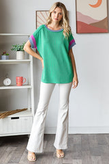 woman wearing a green striped oversized top with purple accents and white flared jeans
