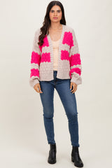woman wearing a light pink cardigan with bold pink patches over a cream top and blue skinny jeans, standing in black ankle boots