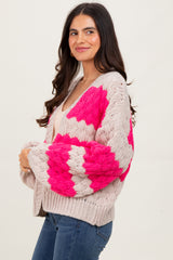 woman wearing a chunky knit cardigan in beige with pink geometric patterns, styled with a light tank top and jeans