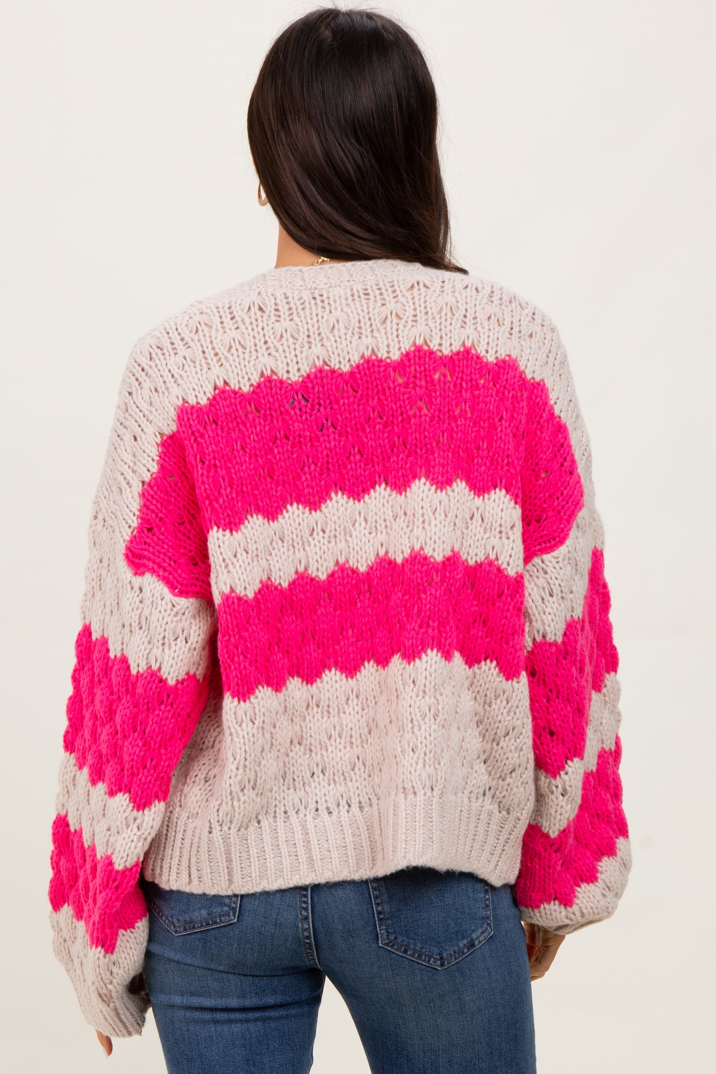 woman wearing a chunky knit sweater with pink and beige stripes, seen from the back, paired with denim jeans