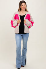 woman wearing a light gray and pink oversized knit cardigan over a black top and blue flared jeans, smiling
