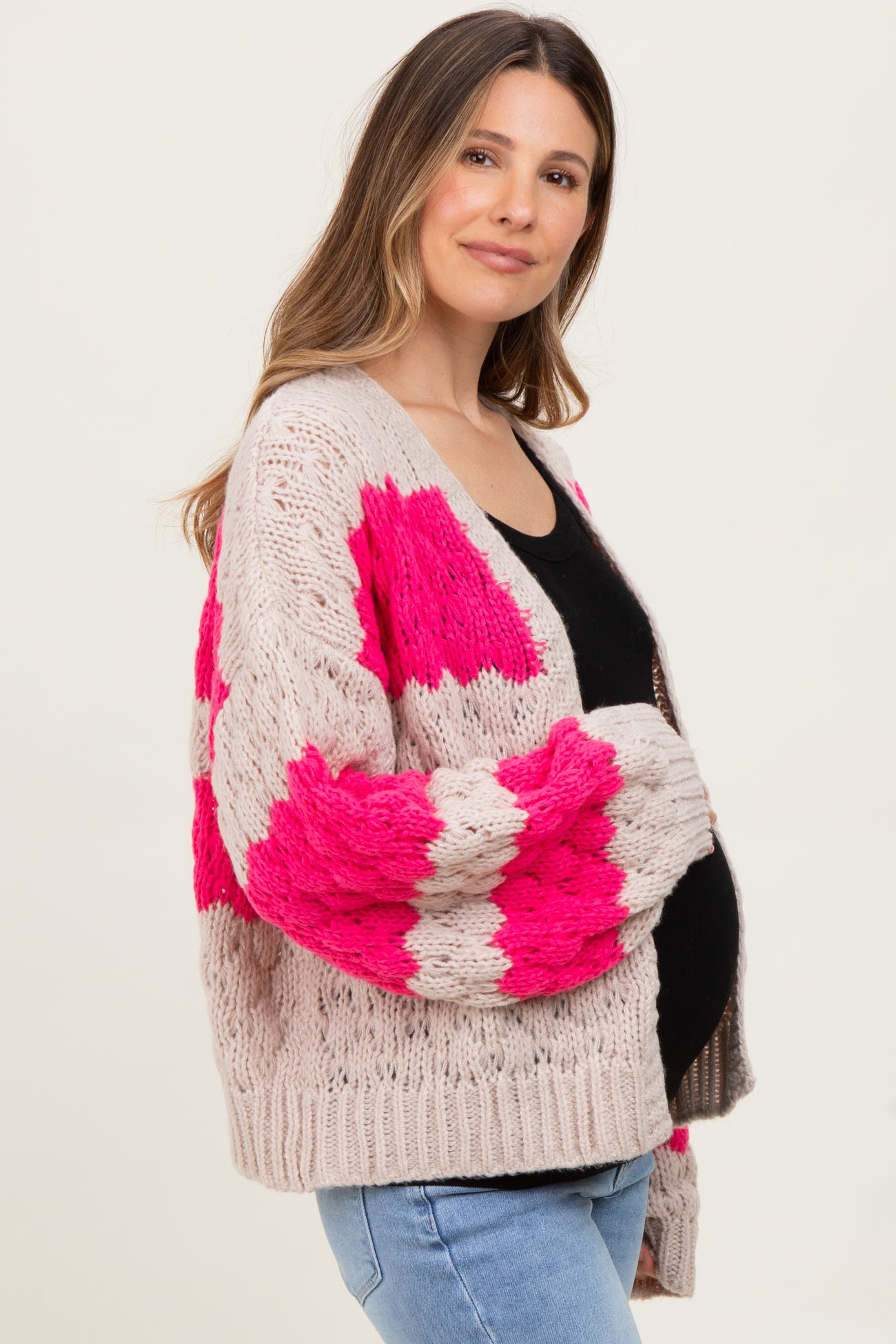 woman wearing a light pink and hot pink patterned maternity cardigan over a black top, with a visible baby bump