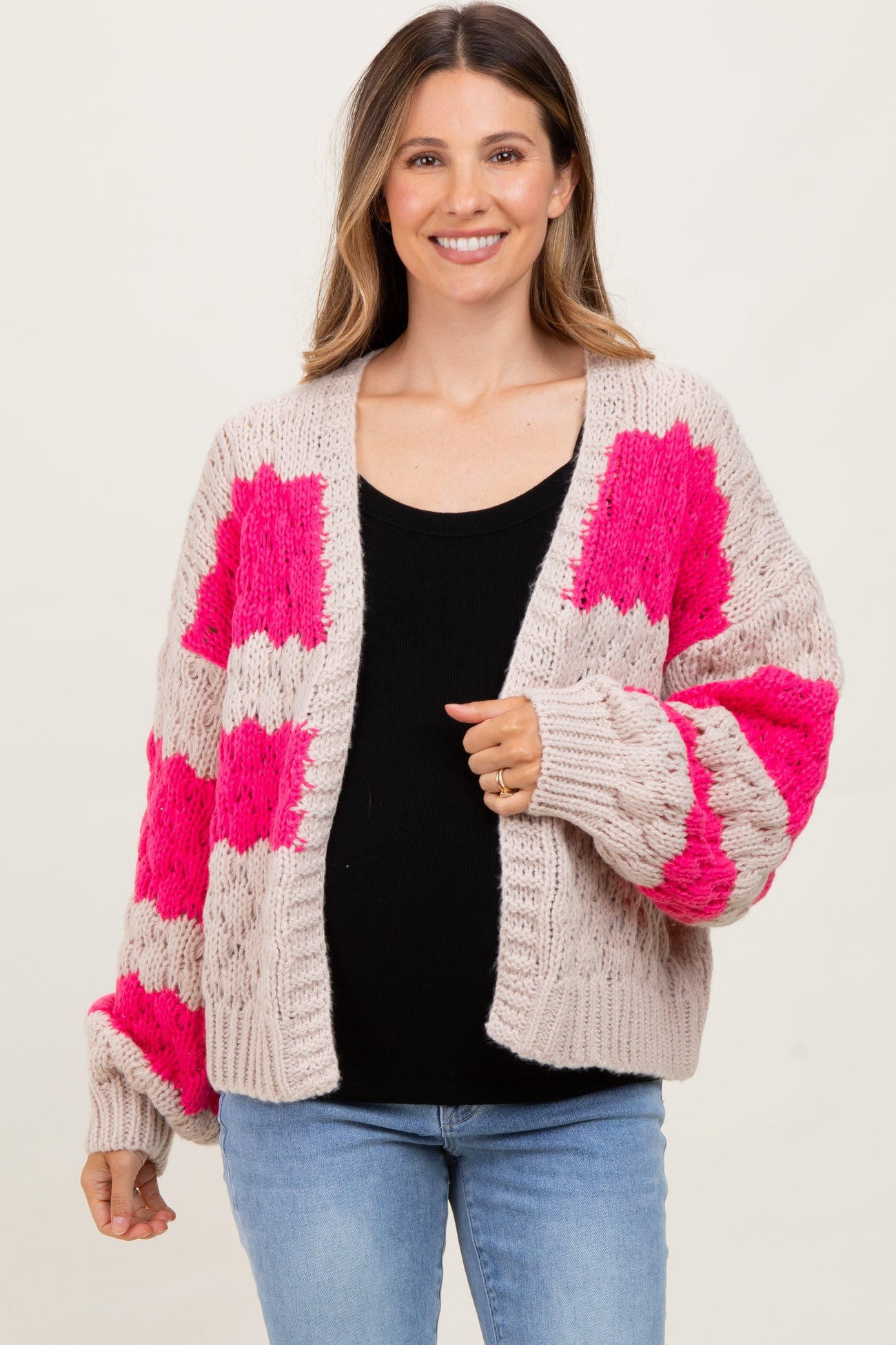 woman wearing a chunky knit cardigan with pink and gray blocks over a black top and blue jeans