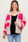 woman wearing a chunky knit cardigan with pink and gray blocks over a black top and blue jeans