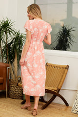 woman wearing a floral pink maxi dress with a smocked back and cap sleeves, standing in a bright indoor setting