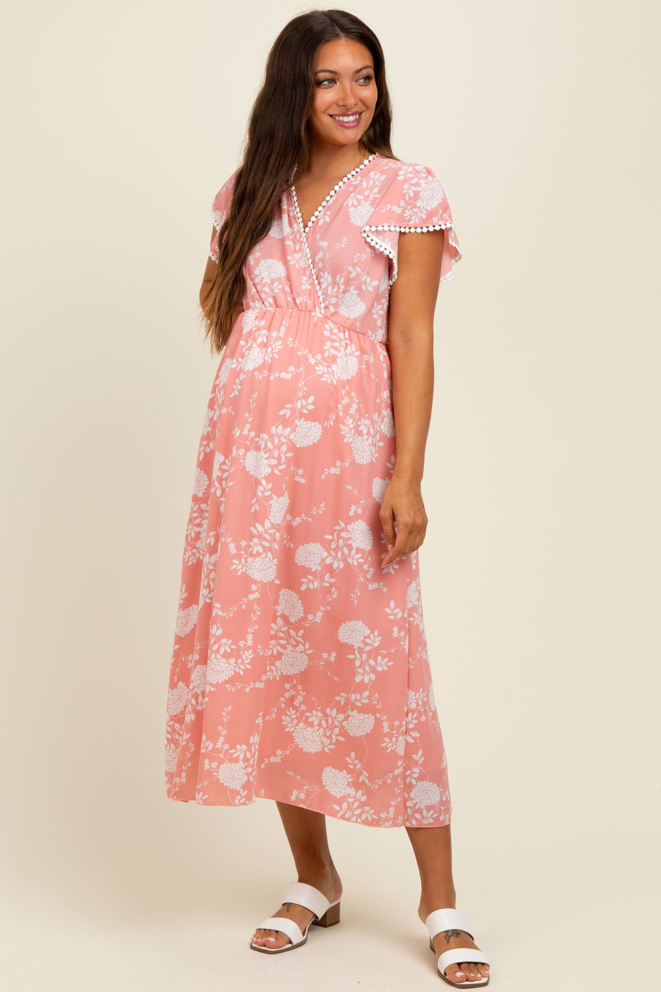 woman wearing a pink floral maternity maxi dress with flutter sleeves and a gathered waist, showing her baby bump