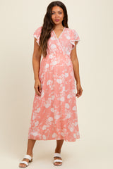 woman wearing a pink floral maternity dress with flutter sleeves and a wrap design, standing against a neutral background