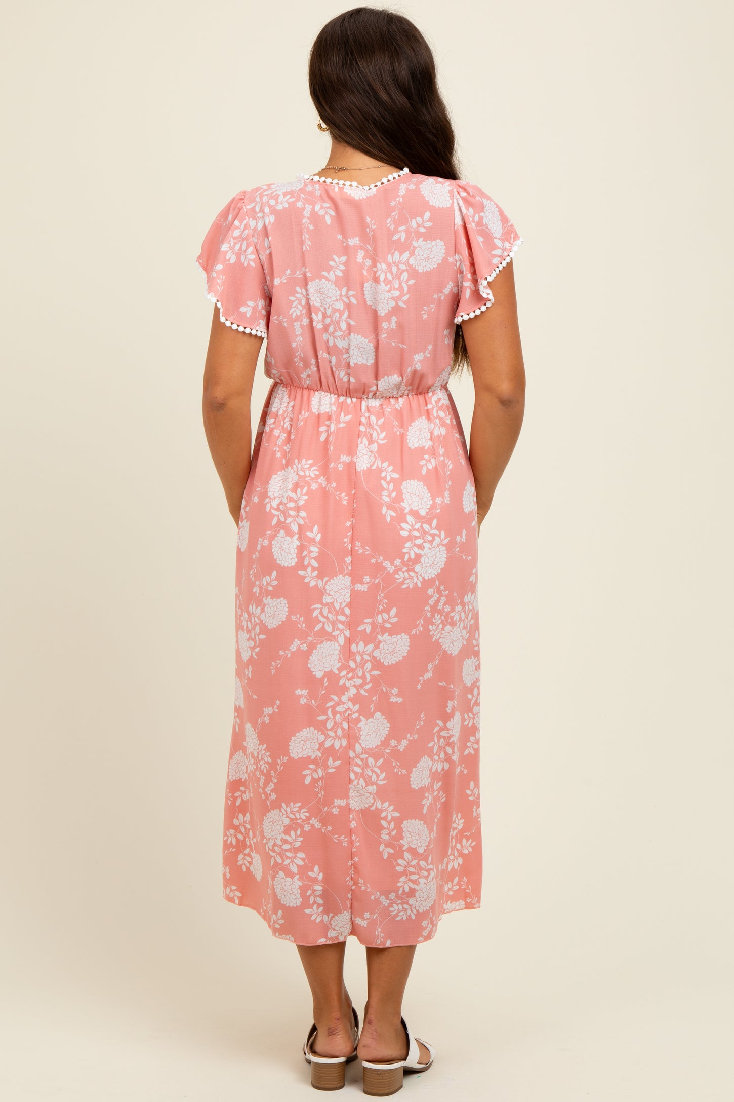 woman wearing a pink floral maternity dress with flutter sleeves and an elastic waistband, viewed from the back