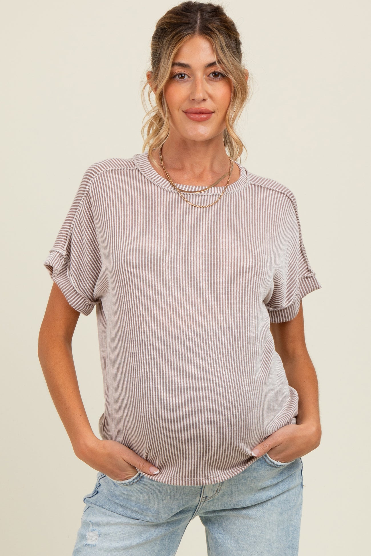 woman wearing a light beige striped maternity top with short sleeves and a visible baby bump