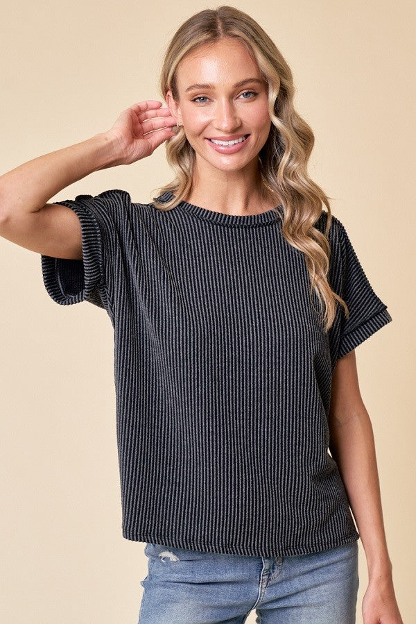 woman wearing a black and white striped short sleeve top, smiling and touching her hair while standing against a neutral background