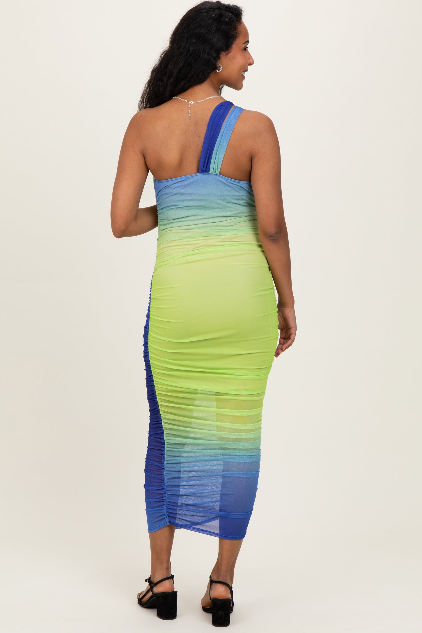 woman wearing a vibrant blue and green one-shoulder maternity dress with a ruched design, showcasing her baby bump