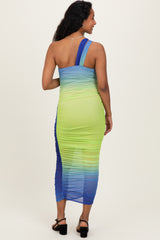 woman wearing a vibrant blue and green one-shoulder maternity dress with a ruched design, showcasing her baby bump