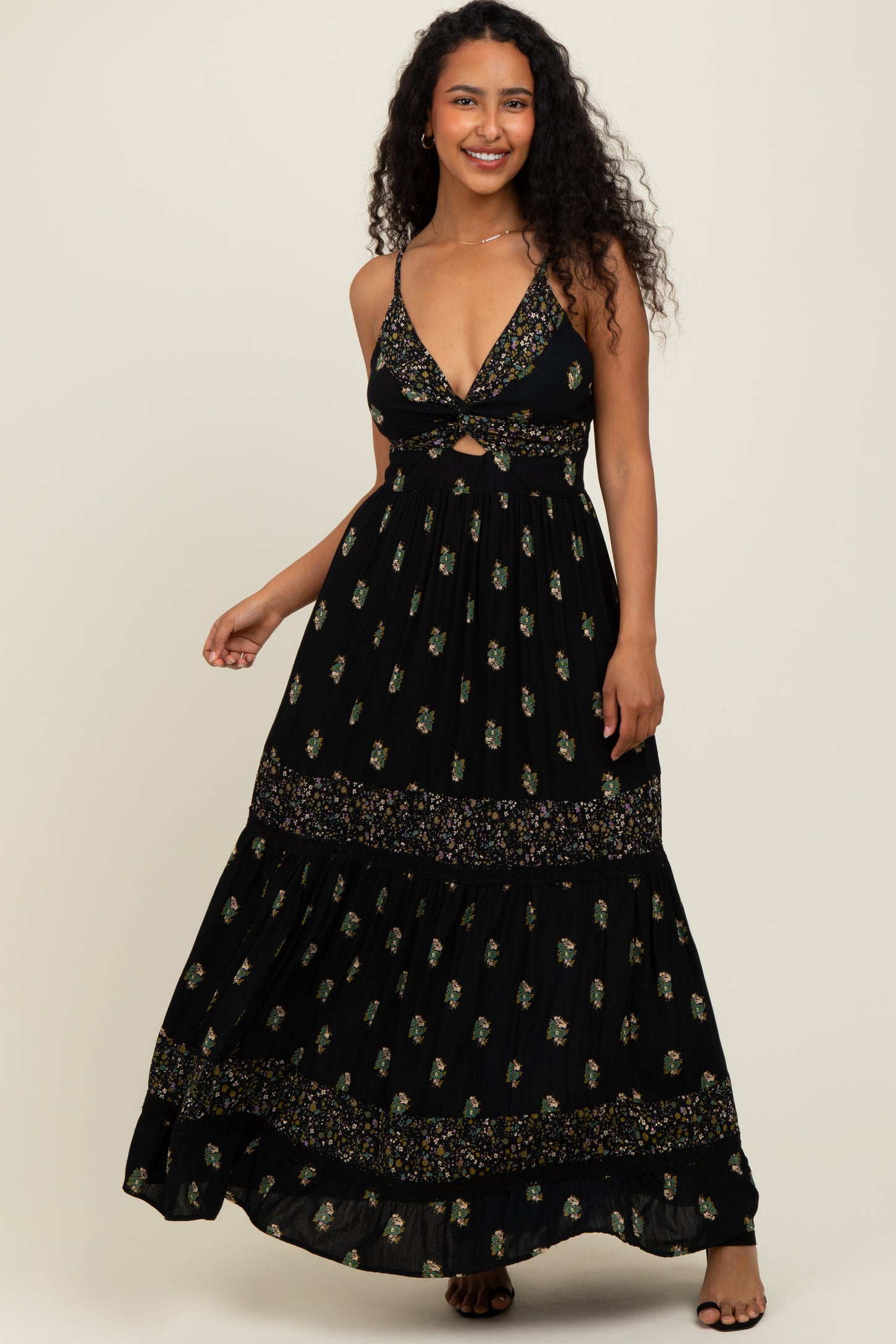 woman wearing a black floral maxi dress with a plunging neckline and cut-out detail, standing against a light background