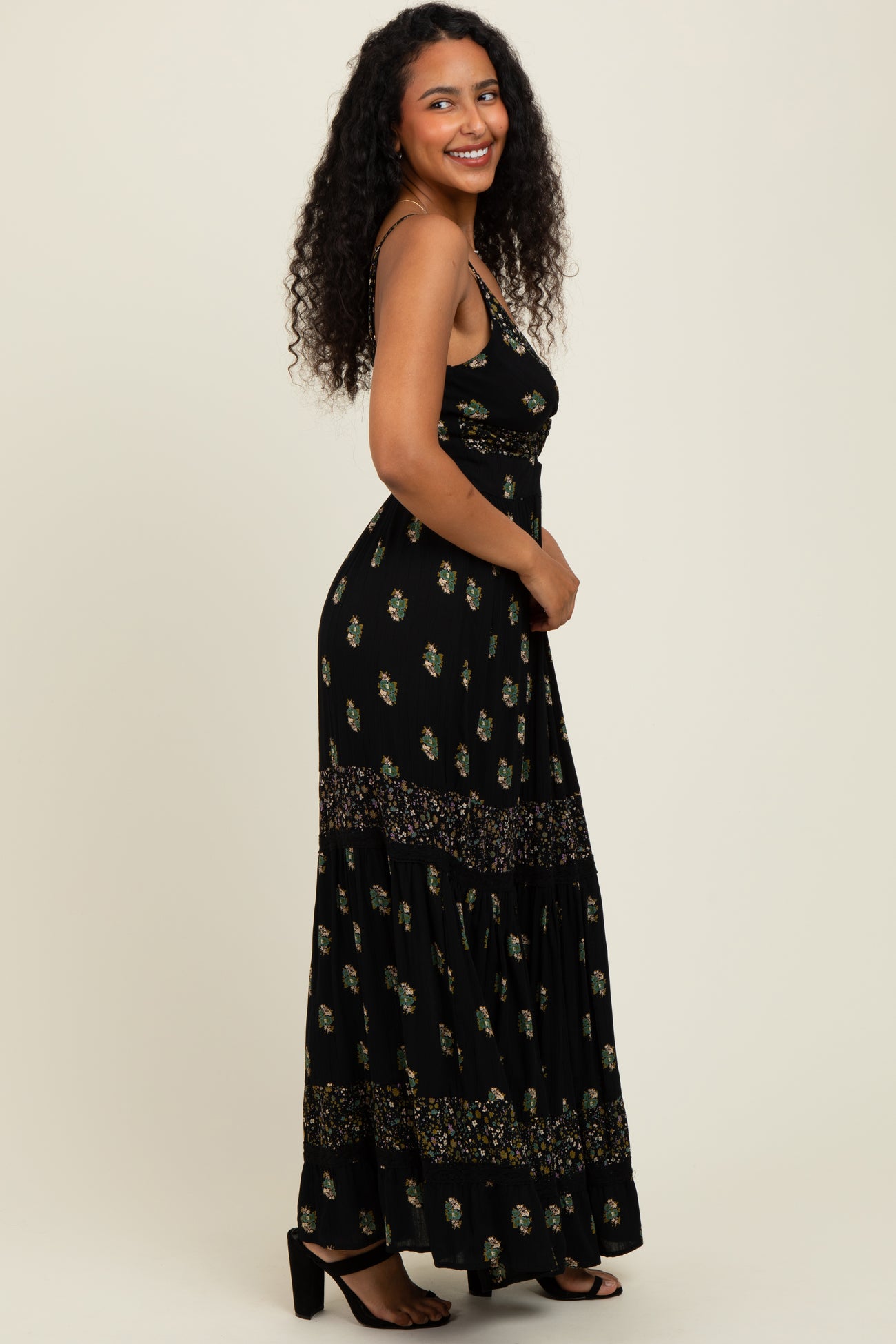 woman wearing a black floral maxi dress with a fitted bodice and tiered skirt, standing against a neutral background