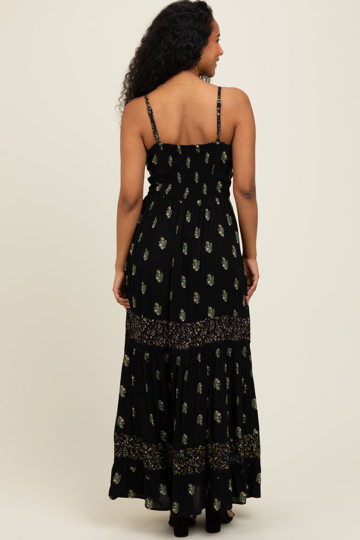 woman wearing a black floral maxi dress with spaghetti straps and tiered detailing from the back