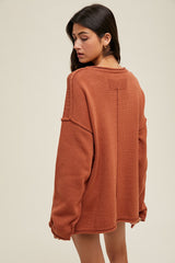 woman wearing an oversized rust-colored sweater with a texture detail and dropped shoulders, facing away from the camera