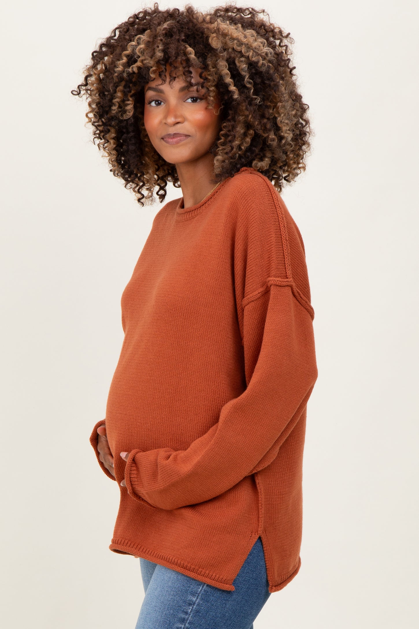 woman wearing a rust colored maternity sweater, showing her baby bump, with long sleeves and side slits