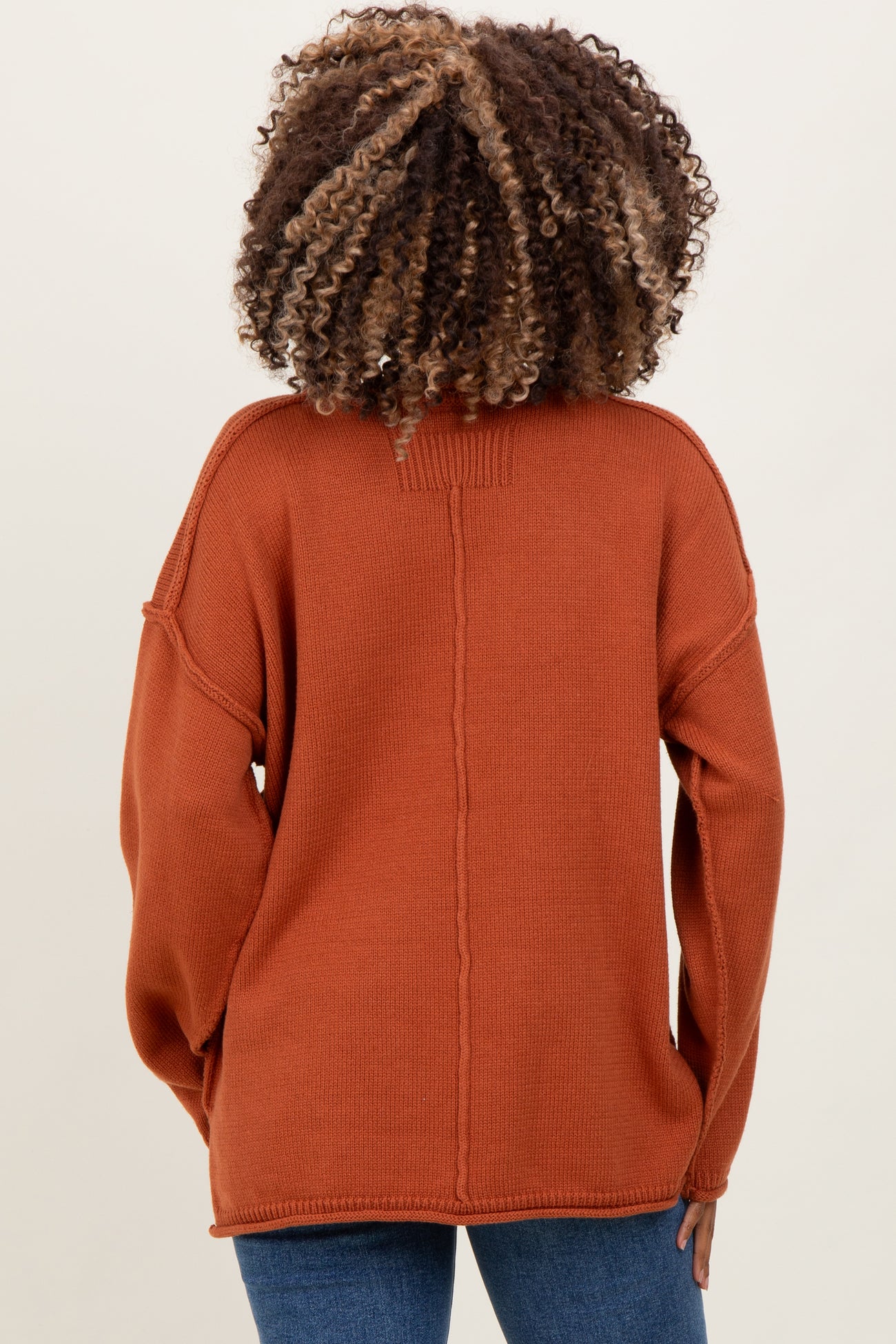 woman wearing a rust-colored oversized knit maternity sweater, view from the back with relaxed fit and dropped shoulders