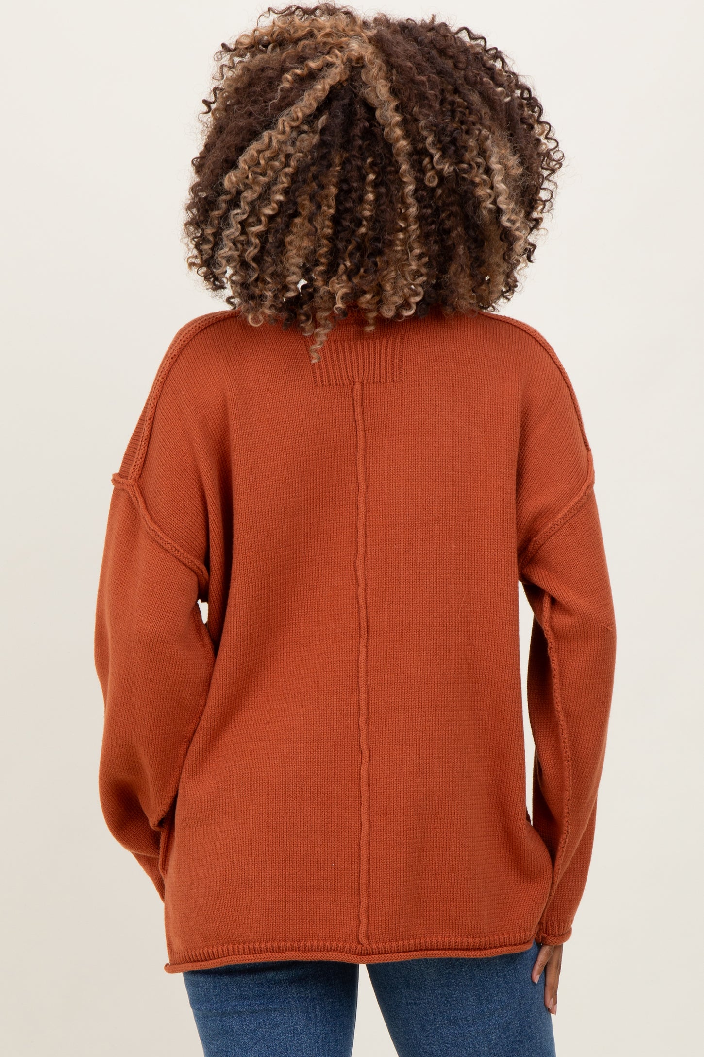 woman wearing a rust-colored oversized knit maternity sweater, view from the back with relaxed fit and dropped shoulders