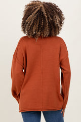 woman wearing a rust-colored oversized knit maternity sweater, view from the back with relaxed fit and dropped shoulders