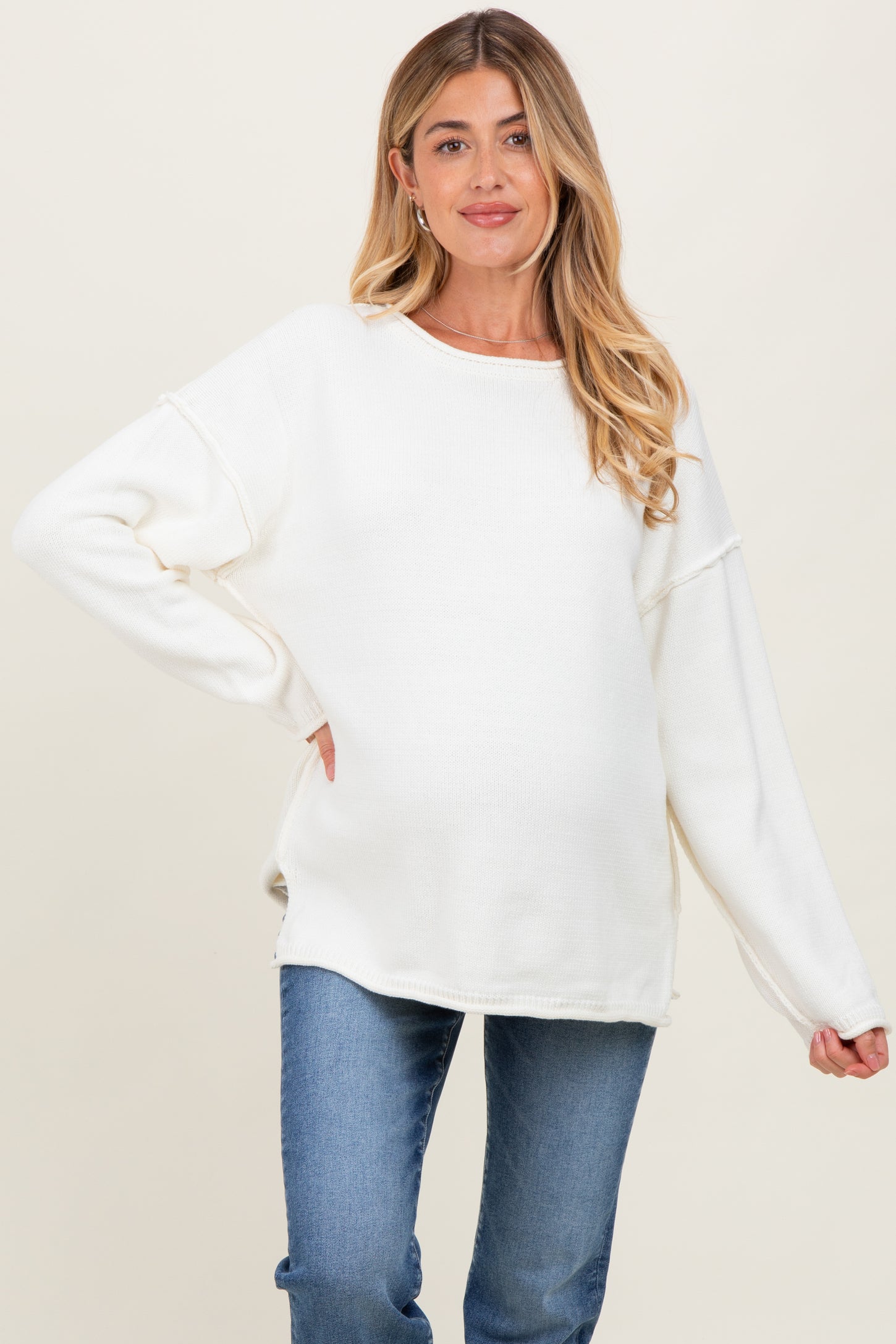 woman wearing a white oversized maternity sweater with relaxed sleeves and a visible baby bump