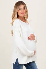 woman wearing a white long sleeve maternity sweater and holding her baby bump