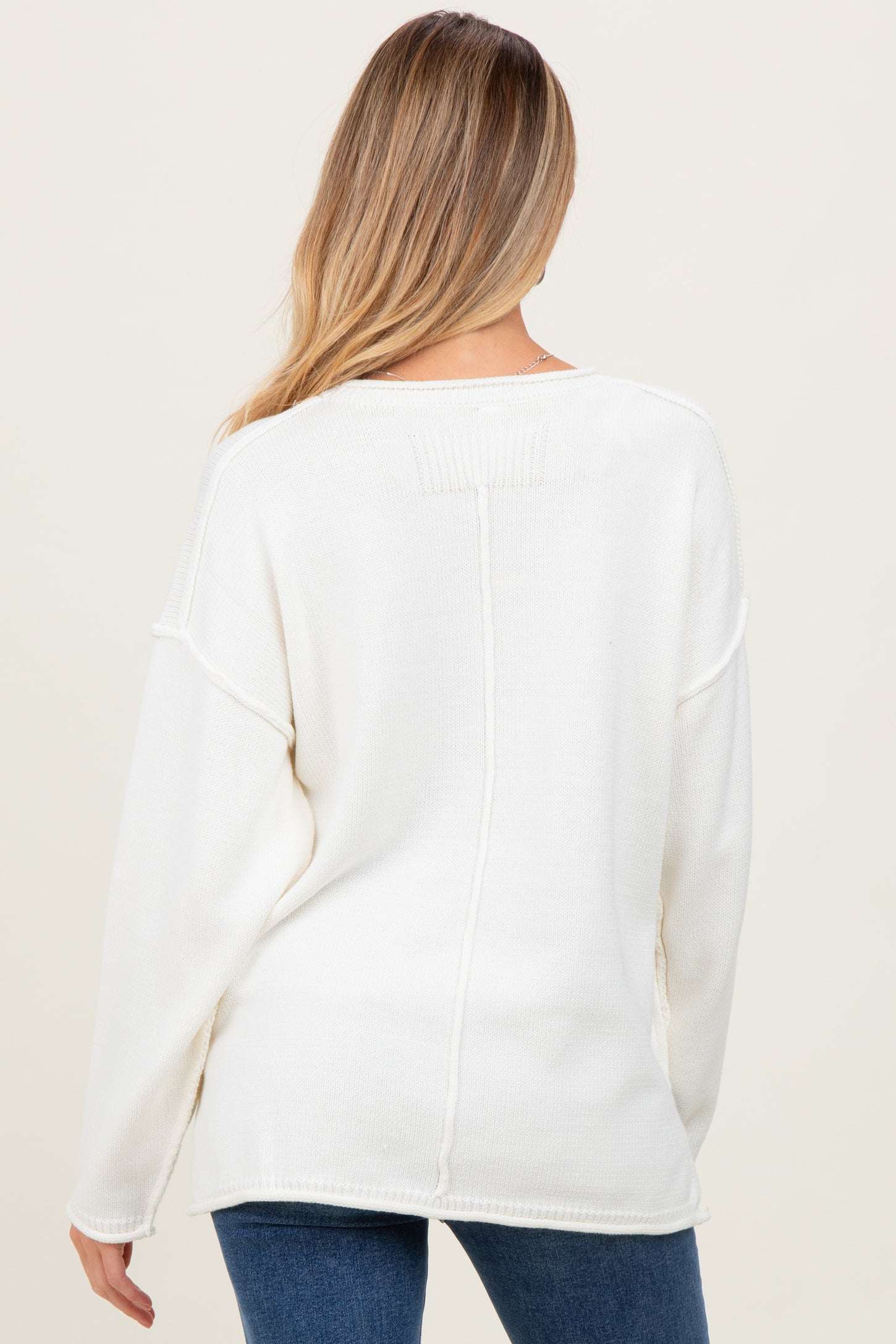 woman wearing a cream oversized maternity sweater with a relaxed fit and long sleeves, viewed from the back