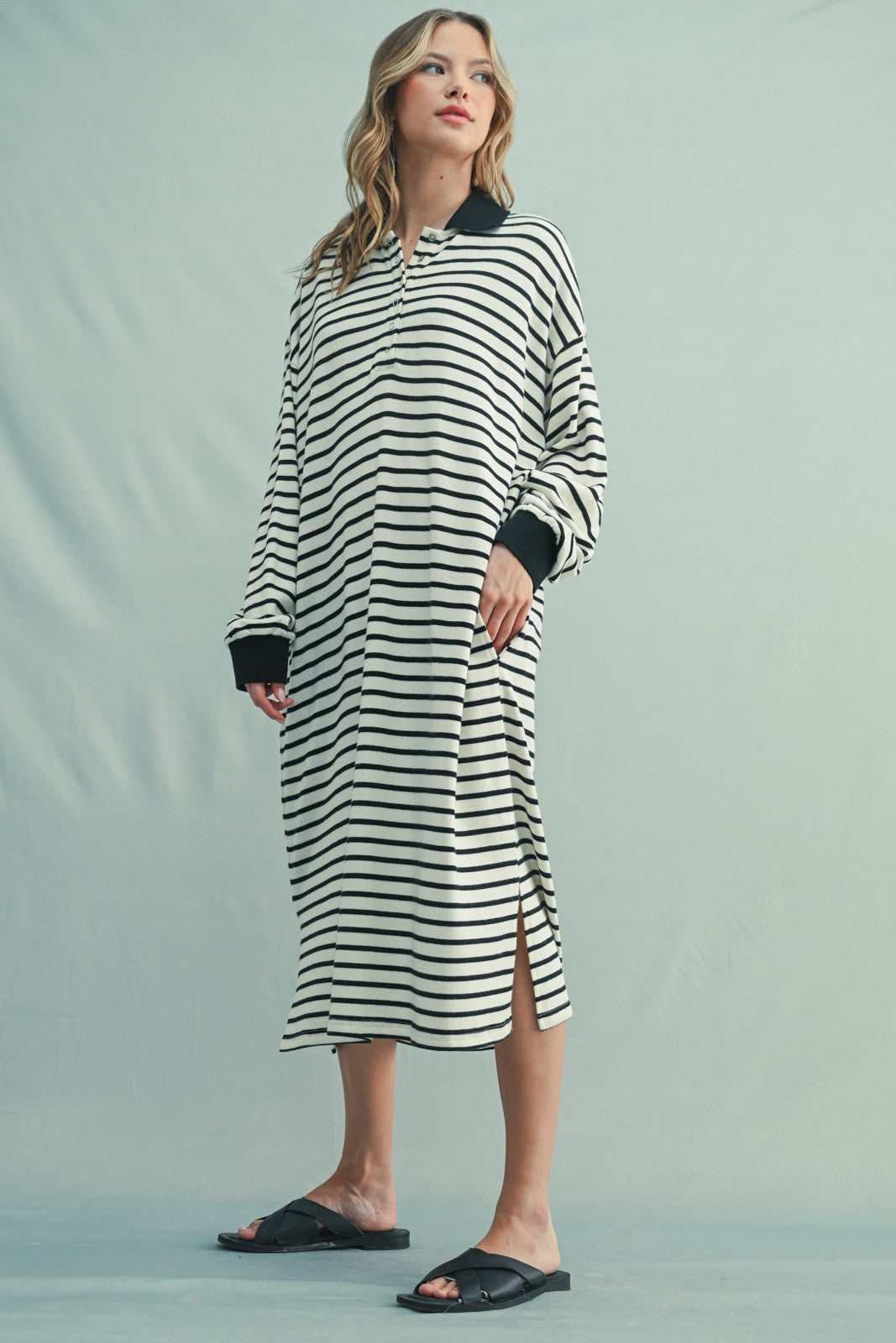 woman wearing a black and white striped long sleeve dress with side slits and black cuffs, standing in slides