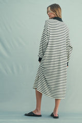 woman wearing a black and white striped oversized dress with long sleeves and side slits, standing with her back turned