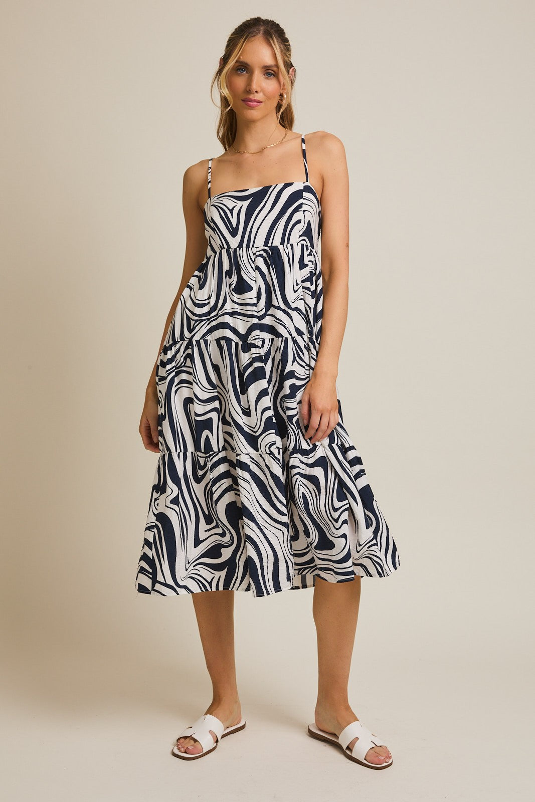 woman wearing a navy and white swirl print midi dress with adjustable spaghetti straps and tiered skirt