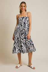 woman wearing a navy and white swirl print midi dress with adjustable spaghetti straps and tiered skirt