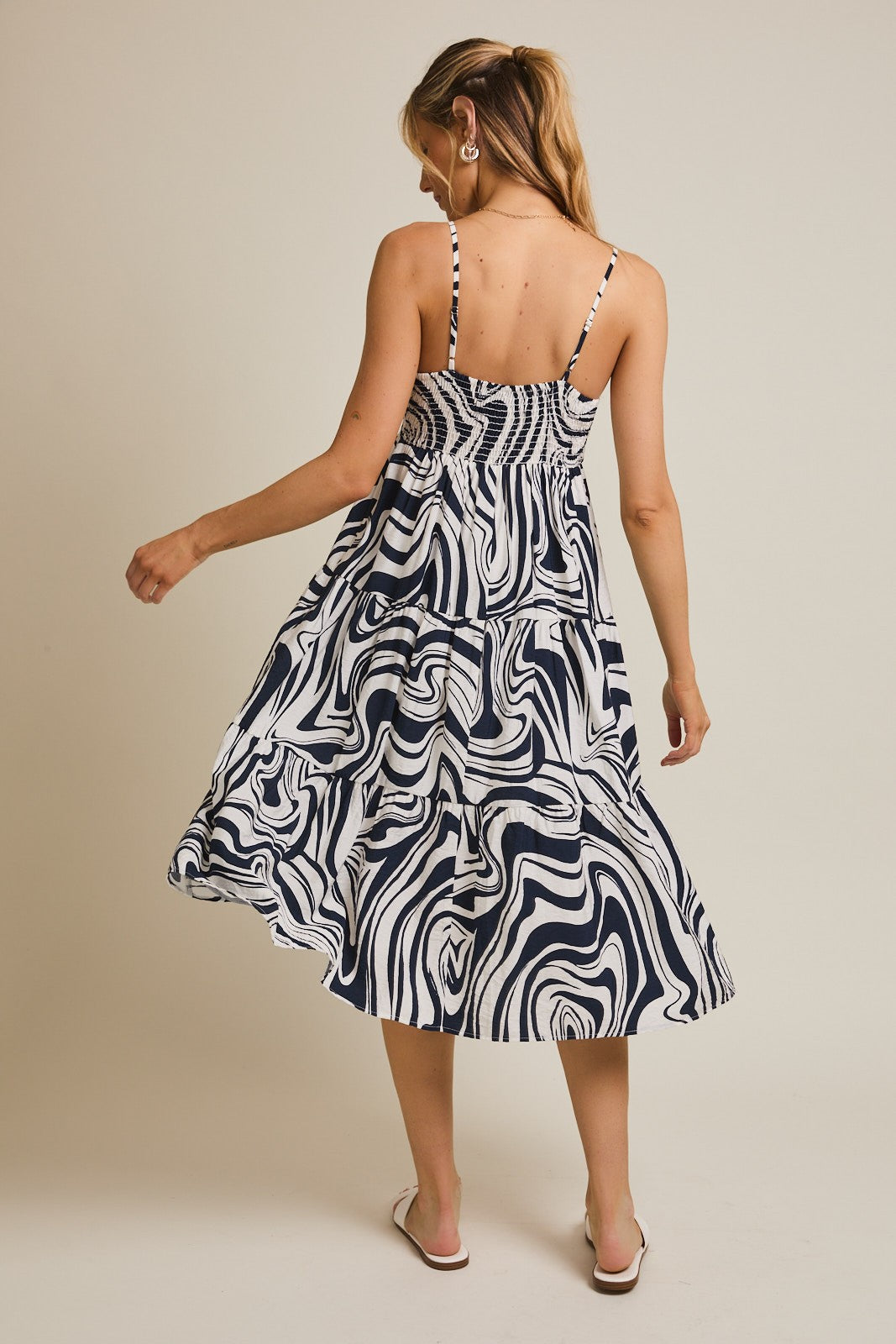 woman wearing a navy and white swirl patterned midi dress with adjustable straps and a tiered skirt