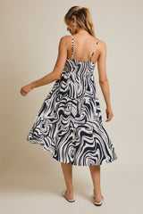 woman wearing a navy and white swirl patterned midi dress with adjustable straps and a tiered skirt