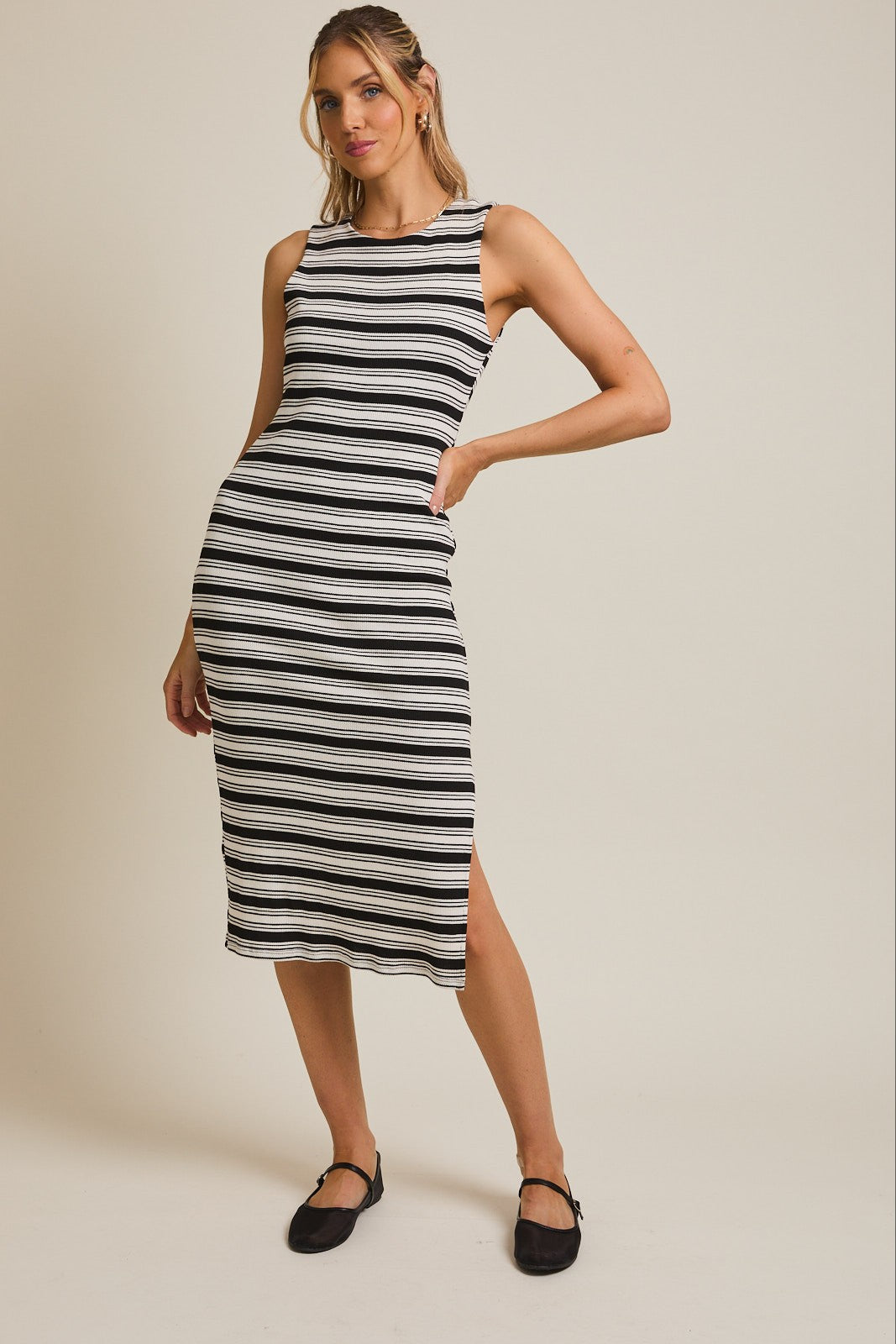 woman wearing a black and white striped sleeveless midi dress with side slit and black flat shoes