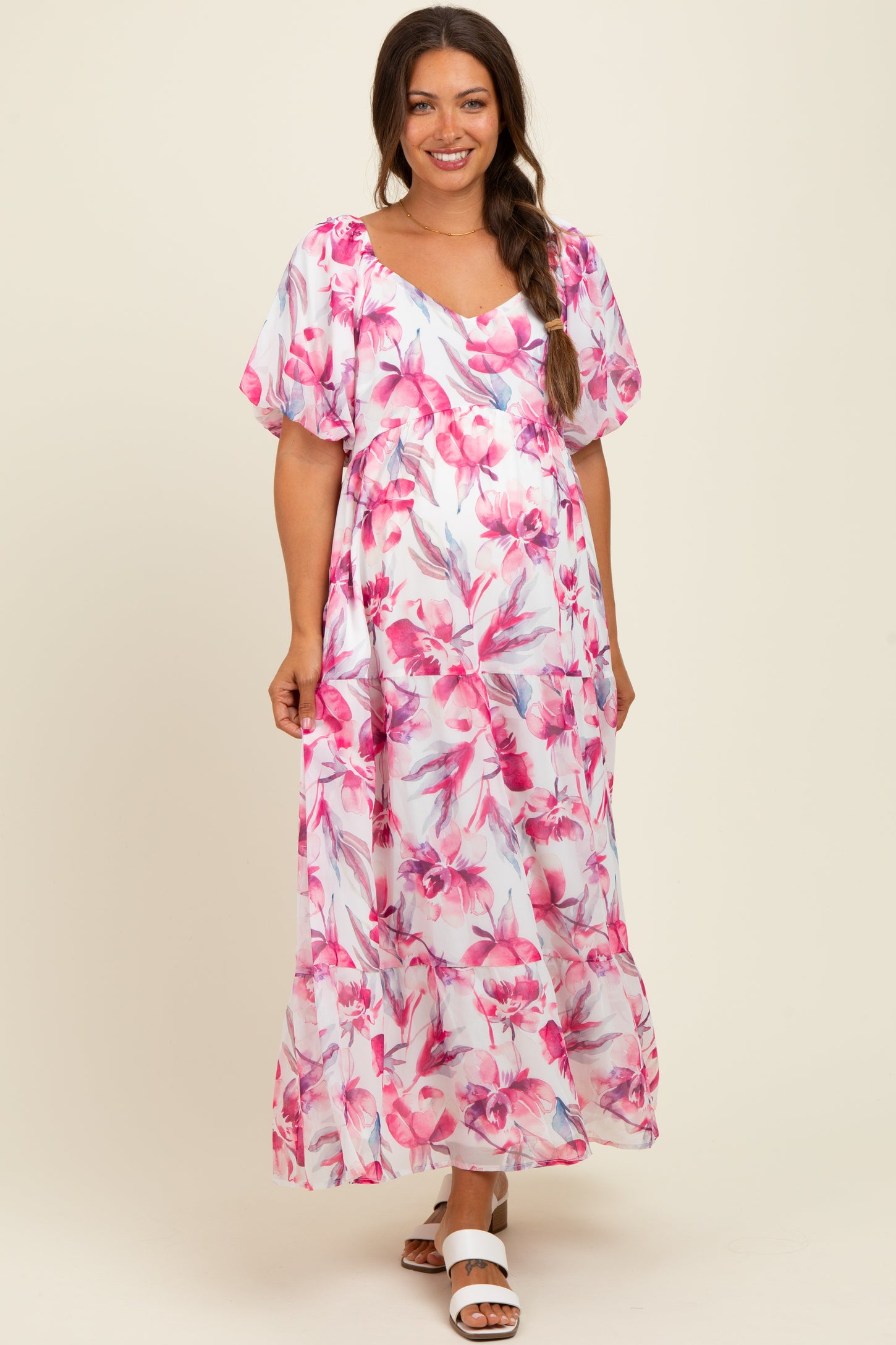 woman wearing a floral pink maternity maxi dress with short puff sleeves and a flowing skirt, showing her baby bump