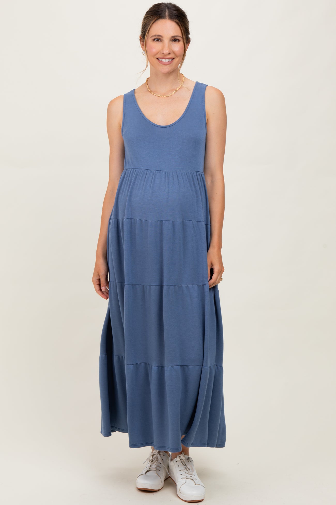 woman wearing a blue sleeveless maternity maxi dress with a flowy tiered design and a visible baby bump