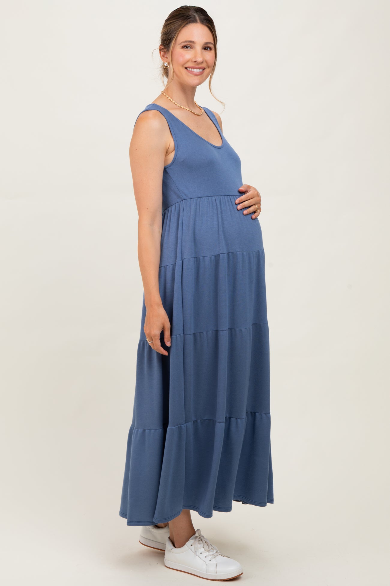 woman wearing a blue maternity maxi dress, showing her baby bump, styled with a flowy tiered design and sneakers